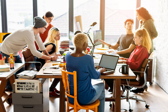 Diverse group collaborating in a modern office with laptops and papers.