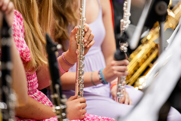 Young flute players hold their silver instruments upright during a school concert band performance, with the gold curve of a saxophone section visible just behind them.  © Jeanne Sager Photo