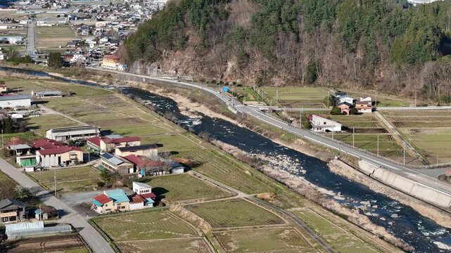 Aerial view shows a rural river flowing beside a road. F lies nearby, surrounded by green fields and trees. The scene is peaceful and quiet, with no people visible. Ideal for agricultural
