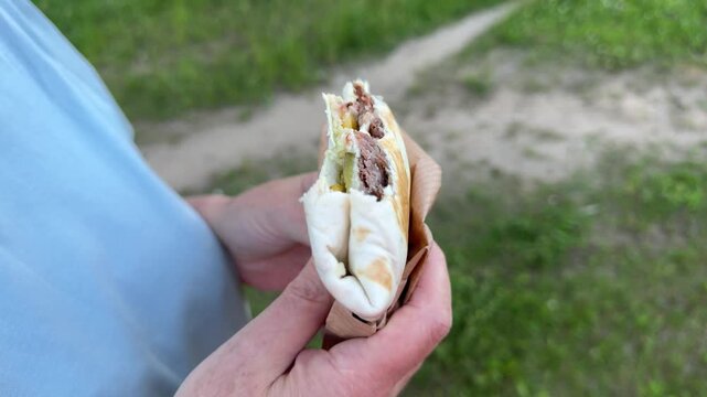 Close-up of a Mexican-style wrap with beef and vegetables held in a hand outdoors, a tortilla sandwich with fresh filling