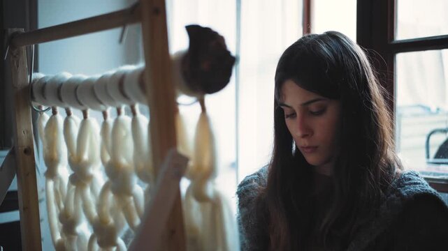 Young Hispanic woman creating a macrame tapestry with wool roving, showcasing handmade textile art, artisan craftsmanship, DIY creativity and bohemian home decor.
