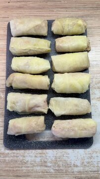 Cabbage rolls on black cutting board closeup, uncooked meat filled cabbage leaves rolled into neat cylinders, arranged in rows