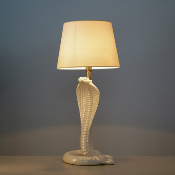 Lit table lamp with white ceramic base in the shape of a cobra.