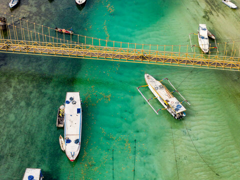 Drone shot of boats anchored in clear turquoise water under a yellow bridge