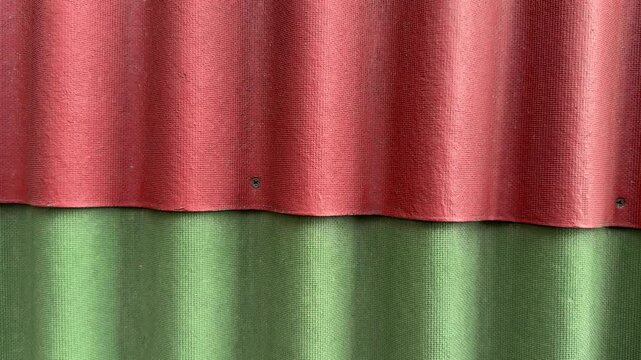 Close-up red and green ondulin tiles highlighting corrugated waves and textured fiber surface, weathered paint and small rust