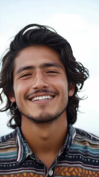 A cheerful male individual with shoulder-length brown locks and a mustache wearing a patterned shirt.