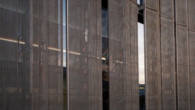 Industrial building facade showcases metallic mesh panels and glass panels creating a reflective modern exterior wall.