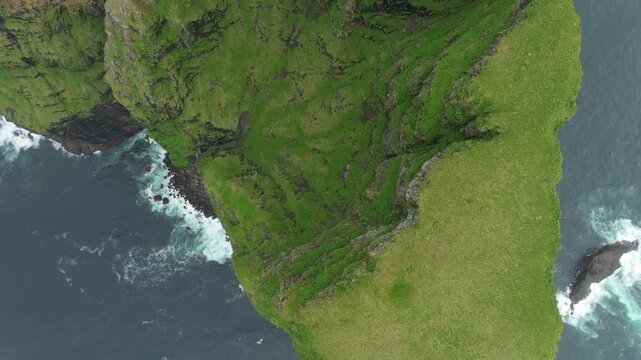 Push in top down aerial drone footage capturing the dramatic, lush green cliffs of mountain Ei&eth;iskollur on the Faroe Islands. Shows the remote island landscape with powerful ocean waves.