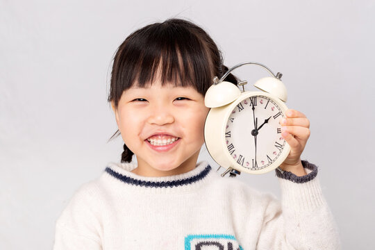 Smiling Asian child holding a white alarm clock, concept of time management, punctuality or waking up early.