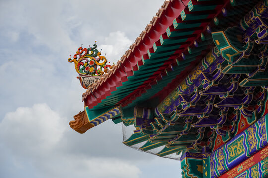 Intricately decorated roof eaves of a traditional Asian temple against a cloudy sky