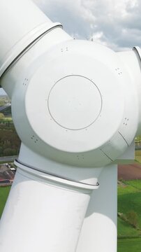 Vertical screen. Wind turbine joint mechanism in motion against a backdrop of green fields and a cloudy sky, highlighting the intricate design and operational aspects of renewable energy systems
