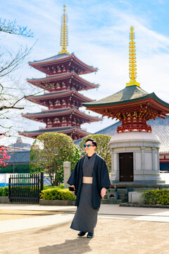 Young smiling Latin man enjoying the moment while holding his smartphone at Sensoji temple in Tokyo Japan, wearing a traditional kimono or yukata, with iconic pagoda and visitors in the background
