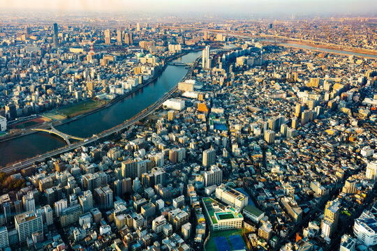 Aerial view of Tokyo from Skytree observatory capturing vast urban landscape, Sumida River, and skyline under warm sunset haze and atmospheric light.
