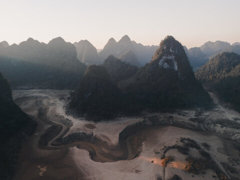 Aerial view of Gods Eye Mountain featuring a distinctive natural rock arch, surrounded by karst limestone peaks and a dry riverbed in the valley, Tra Linh, Cao Bang, Vietnam.