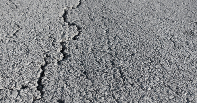 Cracked asphalt road surface. Damaged dark pavement with visible cracks