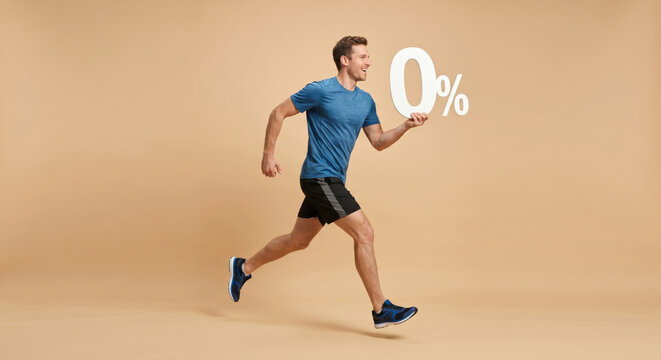 A man runs on a gym floor in sportswear while holding a sign that says zero percent. The setting has a plain background with neutral colors. He appears focused and energetic while exercising