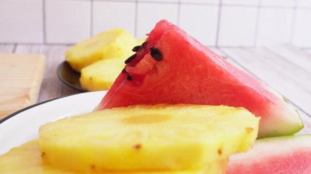 Fresh pineapple slices and watermelon chunks on a rotating plate. The bright yellow of the pineapple contrasts with the red of the watermelon. 