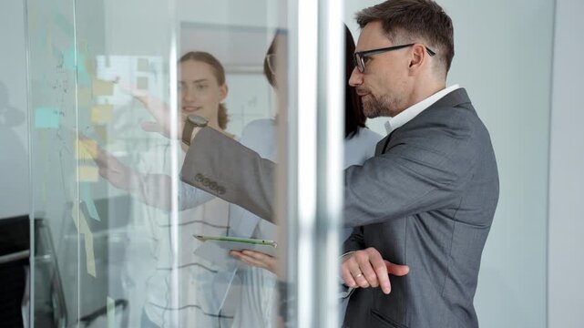 Business team collaborating on strategy, brainstorming ideas with post it notes on a glass board during an office meeting, planning effective project development