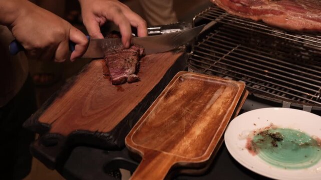 Grill steak meat knife cutting board barbecue beef plate restaurant chef slicing cooked meat on wooden board near hot grate and serving dish in warm rustic kitchen