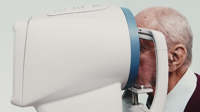 Elderly man undergoing computerized visual field examination using advanced medical equipment in a clinical setting with clear focus on the device and patient interaction