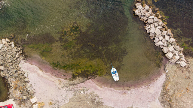 Aerial view of a small white boat moored in a quiet cove with rocky breakwaters and a pebble beach in Lozenets, Burgas, Bulgaria.
