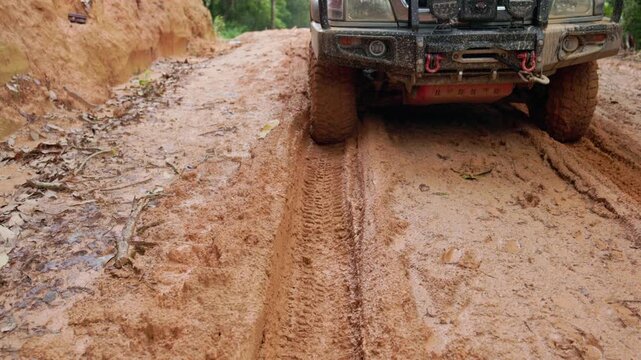 Detailed 4K footage of rugged offroad car wheel rotating in muddy track. Close up of tough tire tread driving through extreme dirt.