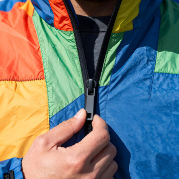Extreme close-up of a hiker's hand zipping up the heavy-duty zipper against brightly colored, crinkly ripstop nylon fabric.