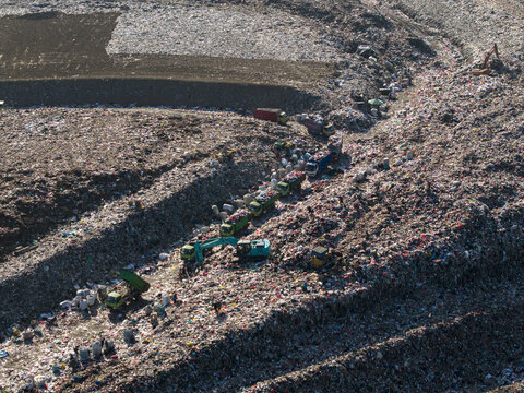 Aerial view of TPA Suwung landfill showing trucks and excavators operating amidst vast piles of waste in Kecamatan Denpasar Selatan, Bali, Indonesia.