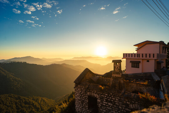 Aerial view of Chakrata hill station featuring a stone building with a modern upper level overlooking Himalayan mountains during sunset in Chakrata, Uttarakhand, India.