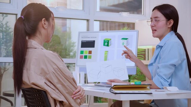Two asian businesswoman working packaging design with ai computer, team business woman meeting of paper sketch drawing mockup holding prototype product box, creative packaging design project.