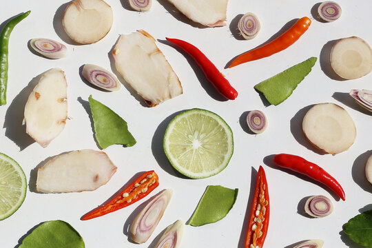 A colorful, close-up pattern of Thai herbs: lime slices, galangal, lemongrass, chilies, and kaffir lime leaves.