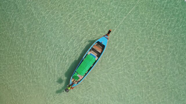Longtail boat floating on the shallow, pristine turquoise waters of Phuket coast, Thailand, reflecting clear blue sky and inviting travelers to explore the tropical paradise. Aerial view top down shot