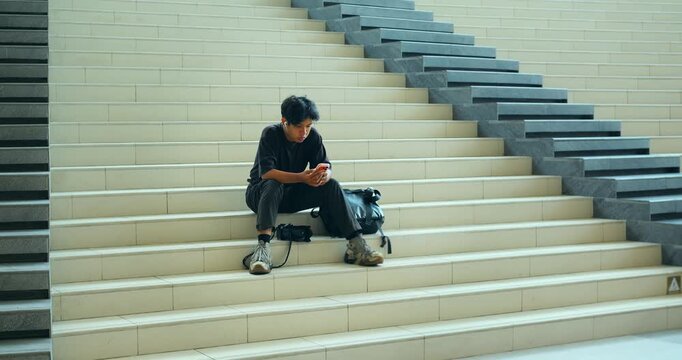 Young man sitting on wide staircase using smartphone, backpack beside him, repeated across frames while waiting alone on modern indoor steps with geometric lines and clean architectural setting