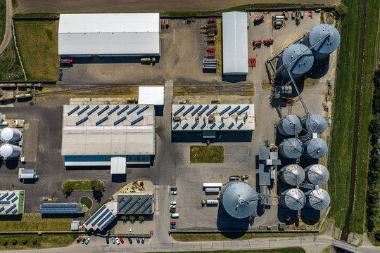 Aerial view of an industrial facility featuring large grain silos, warehouses with solar panel arrays, and paved storage areas in Slavkov u Brna, South Moravian Region, Czechia.