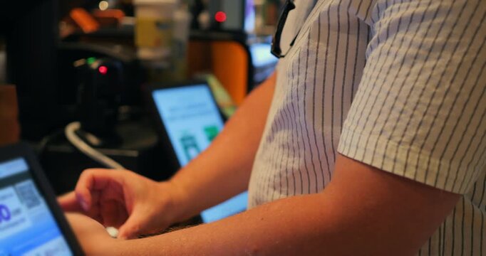 Person using smartphone for mobile payment at checkout terminal in cafe, tapping screen beside card reader and point of sale device, close up of hands during contactless transaction at counter
