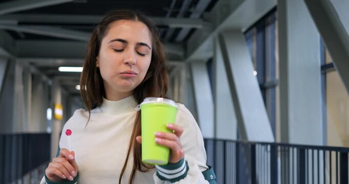 Casual traveler enjoying morning coffee. Individual sipping hot drink in bright glass corridor environment. Person wearing casual clothing taking quick coffee pause in welllit environment