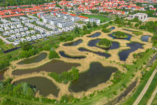 Aerial view of interconnected ponds and wetlands with reeds and small islands, near a modern residential area in Slavkov u Brna, South Moravian Region, Czechia.