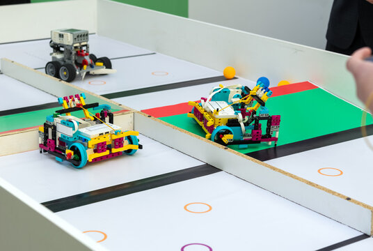 Brightly colored plastic constructor robots on a multi-lane race table. Close-up of turquoise, yellow, and magenta educational robots aligned in lanes on a white competition table with colored marking