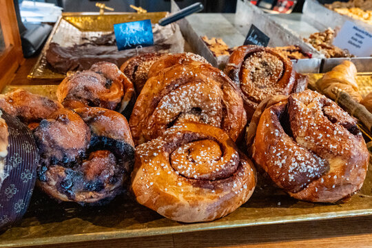 Delicious, sweet, glazed, large cinnamon and cardamom spiced sweet pastry buns (Kanelbullar or Kanelbulle), brushed with egg glaze, topped with white pearl-sugar sprinkles freshly baked for Fika