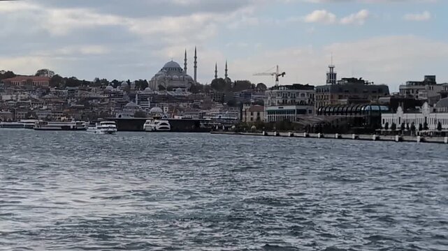 Turkish flag waving on a boat navigating the Bosphorus strait with the Istanbul skyline featuring the Suleymaniye Mosque in the background on a cloudy day