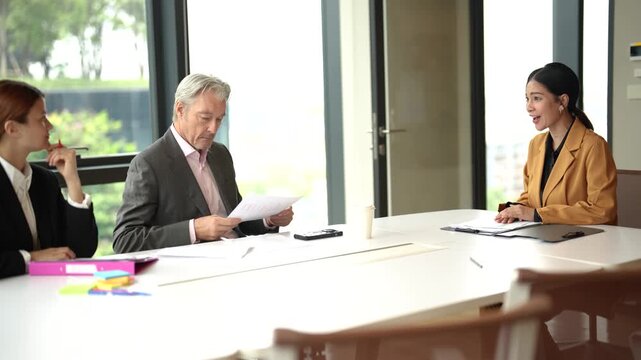 Professional sales representative explains business proposal and hands printed documents to each business partner during corporate meeting. Collaboration, negotiation in modern office.
