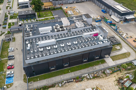 Aerial view of an AI data center featuring numerous HVAC cooling units on the roof, surrounded by a parking lot and industrial facilities in Warsaw, Masovian Voivodeship, Poland.