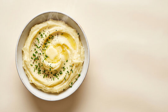 Creamy mashed potatoes with melting butter slice and chopped chives in bowl top view copy space
