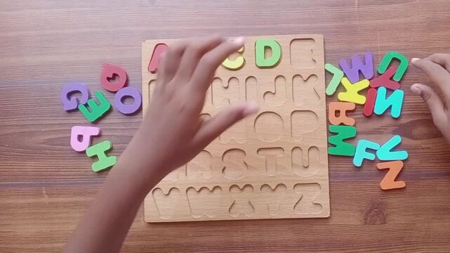 Child hand arranging and playing with colorful wooden alphabet puzzle board for early learning and education on white background.