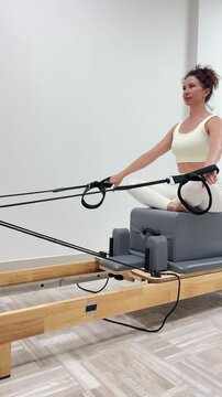 Pilates reformer workout woman doing exercise on gym machine for core strength and flexibility in bright minimalist studio setting