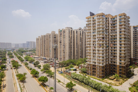 Aerial view of a modern residential apartment complex with tall buildings, a wide road, and lush greenery in Greater Noida, Uttar Pradesh, India.