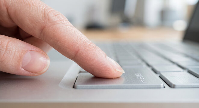 Close up of human finger pressing enter button on silver laptop keyboard, technology and internet concept.
