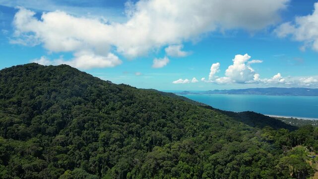 Aerial drone footage descending from a mountain over a dense tropical forest near Thong Nai Pan, Koh Phangan, Surat Thani, Thailand, on Thursday, July 2, 2026. The smooth downward movement reveals the