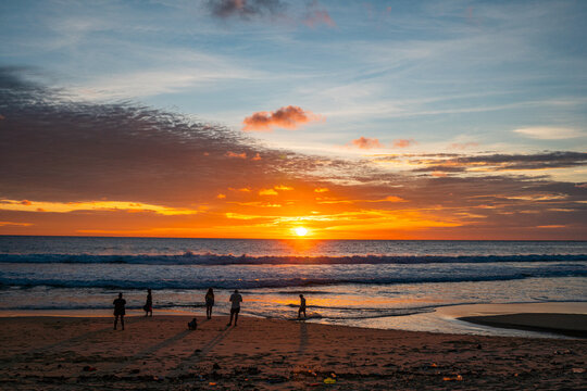 Stunning tropical beach sunset with glowing orange skies, gentle ocean waves, and peaceful island silhouettes creating a serene coastal atmosphere.