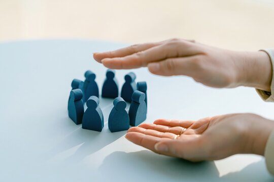 A womans hands protecting a group of wooden figurines in a circle on a blue table, depicting a gentle and caring atmosphere for community and humanism concepts